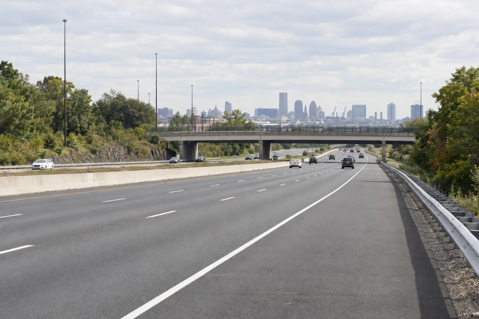 A divided highway with a broad shoulder, guardrails, and an overpass.
